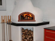 Ein weisser Pizzaofen in einer Küche, es wurde eingefeuert und das Holz brennt.